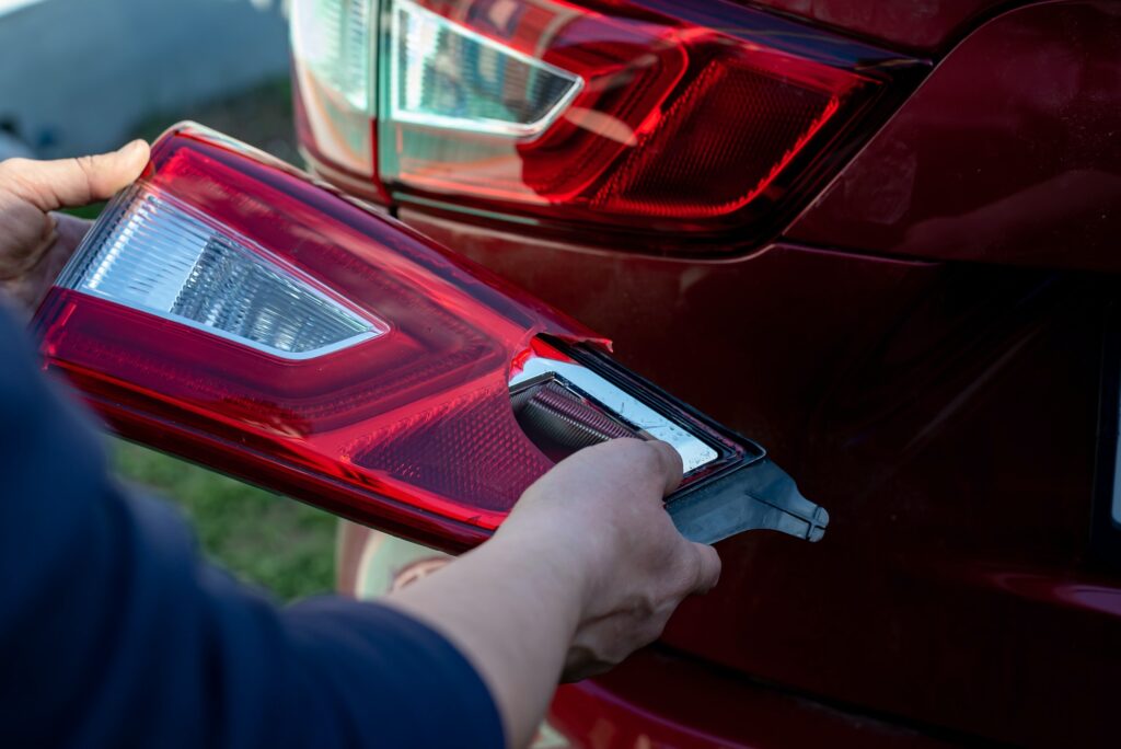 Zoom em mãos de mecânico comparando as peças para trocar de farol de carro.