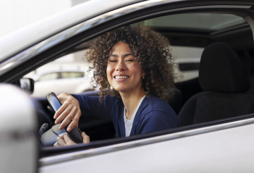 Mulher sorridente dentro de carro, olhando pela janela. 