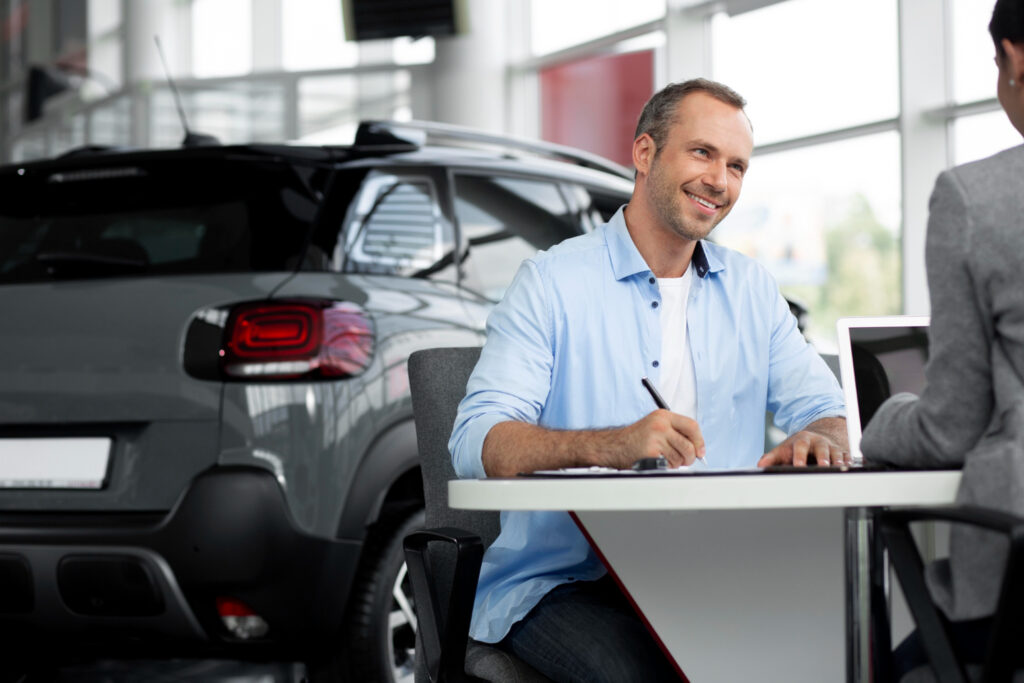 Rapaz assinando contrato em uma loja de automóveis